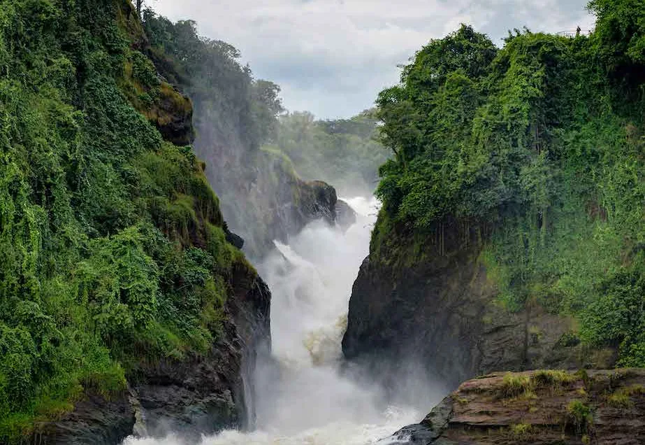Dramatic waterfall surges between lush, green cliffs under a cloudy sky, creating misty splashes.
